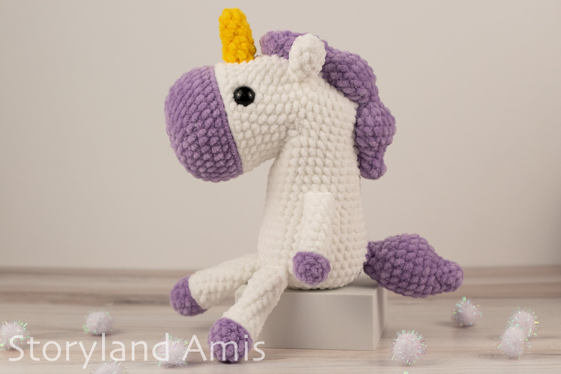Crocheted unicorn toy with a purple body and yellow horn on a light wooden floor.