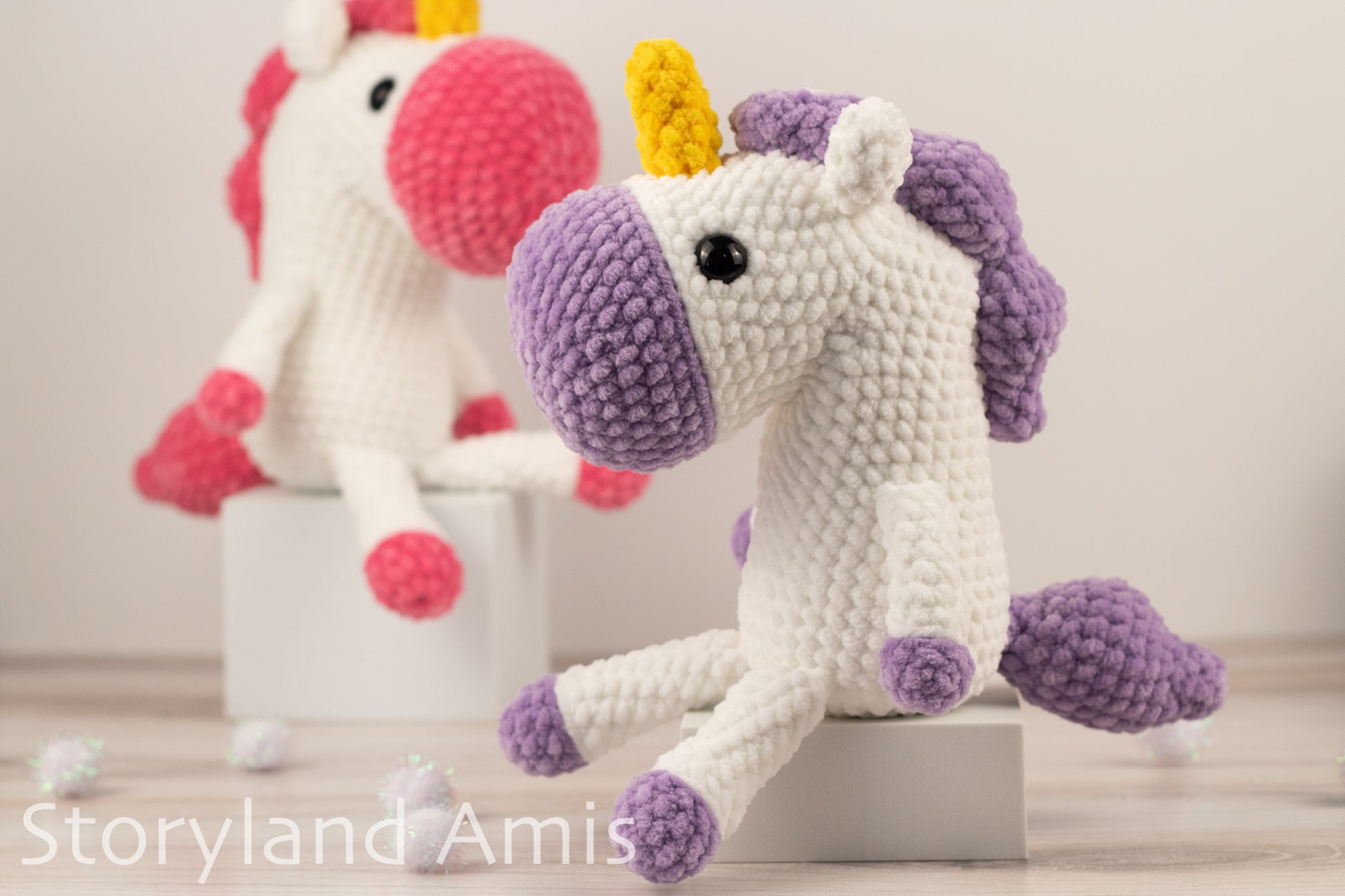 Two crochet unicorns, one pink and one purple, on a light background with 'Storyland Amis' branding.