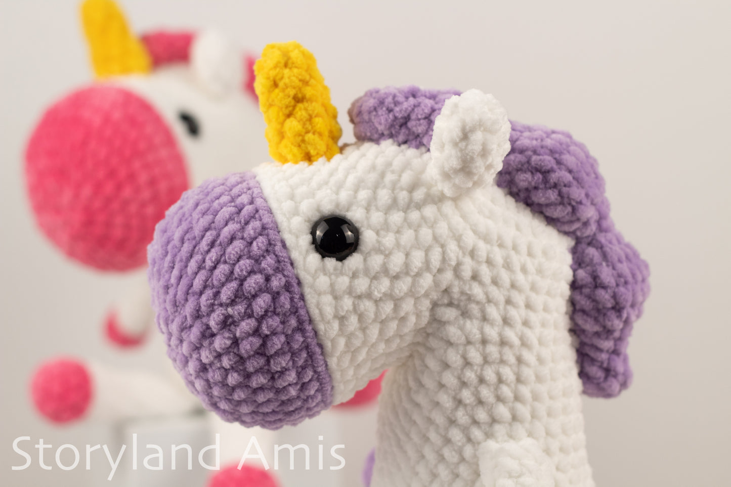 Crocheted unicorn toy with a purple mane and yellow horn on a light gray background.