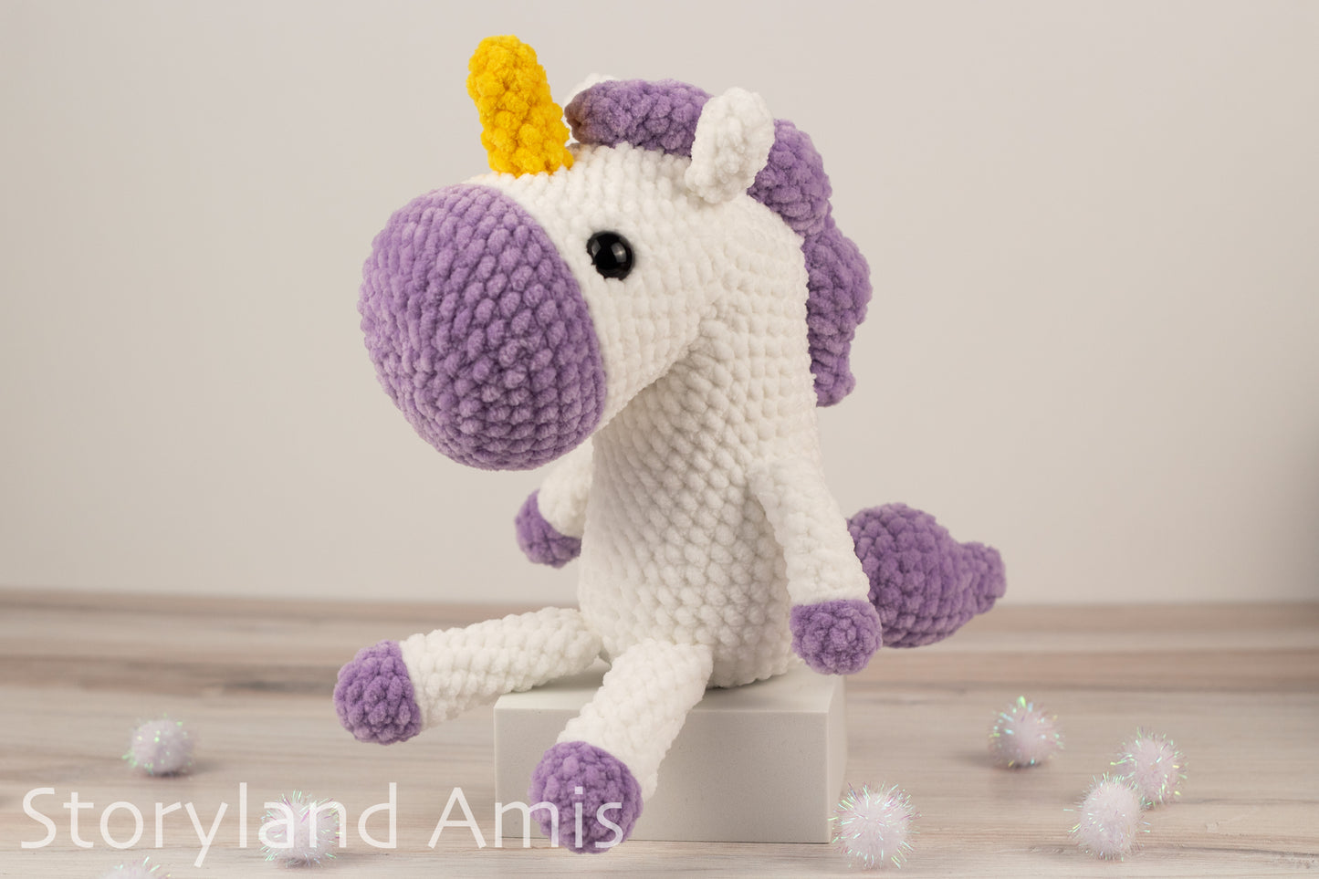 Crocheted unicorn toy with purple mane and hooves on a light wooden surface.