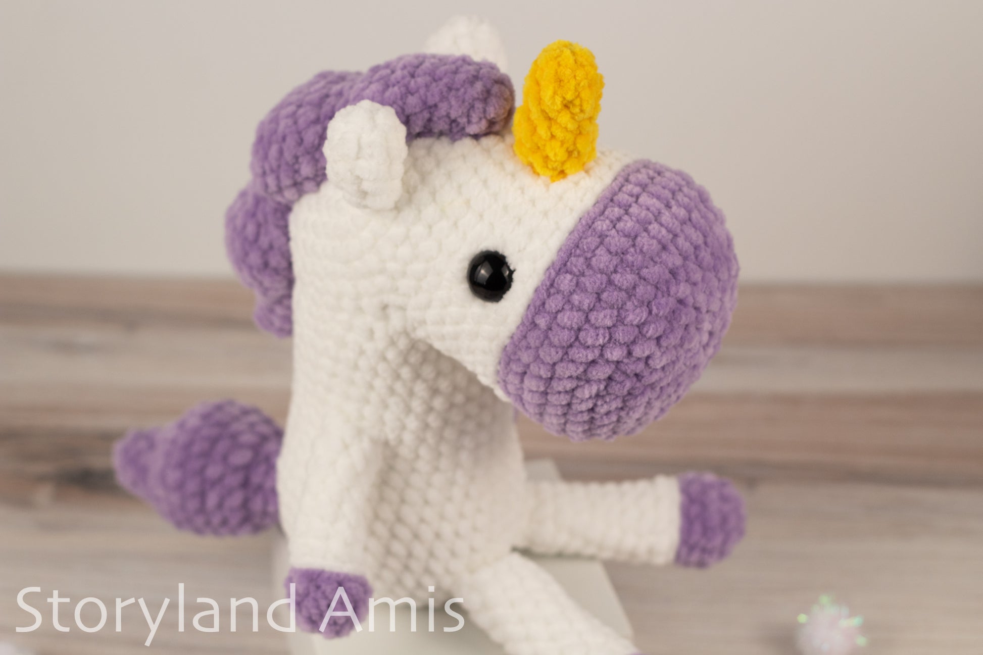 Crocheted unicorn toy with purple mane and yellow horn on a wooden surface.