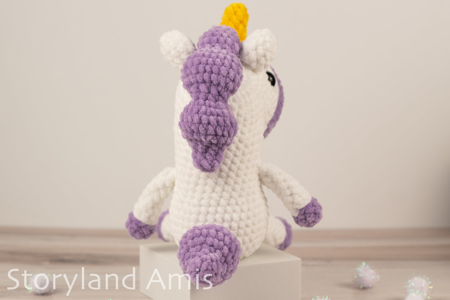 Crocheted unicorn toy with purple mane and feet on a white background