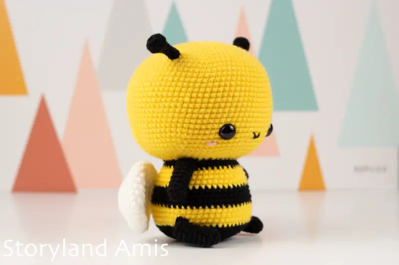 Crocheted bee toy with a happy expression against a colorful geometric background
