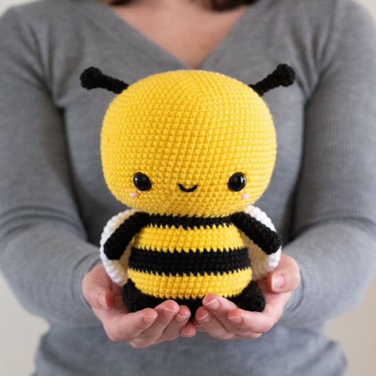 Person holding a yellow and black crochet bee toy against a neutral background