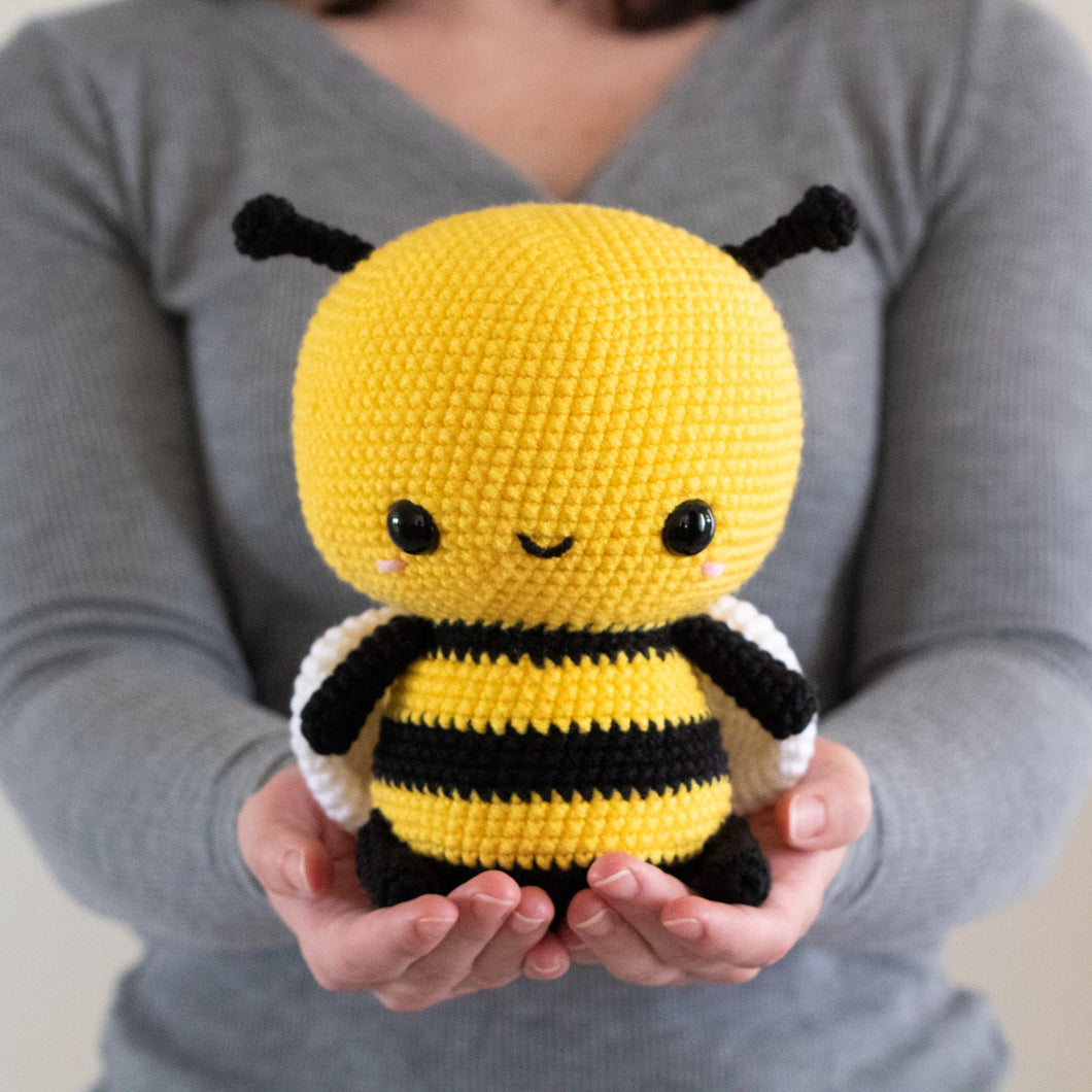 Person holding a yellow and black crochet bee toy against a neutral background