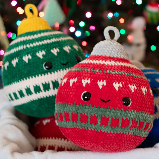 Three crocheted Christmas ornaments in green, red, and blue with a blurred festive background.